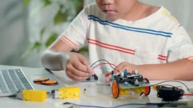 Asyalı çocuk, Arduino robot arabasıyla sensör çipine enerji ve sinyal kablosu takıyor, küçük çocuk oyuncaklarla uzaktan öğreniyor, STEAM eğitim teknolojisi dersleri.