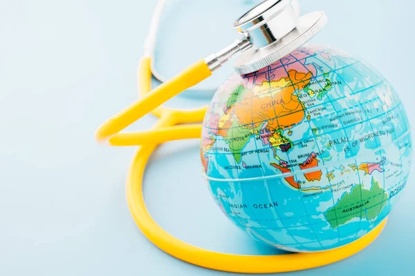 World Health Day. Top view yellow doctor stethoscope wrapped around world globe isolated on pastel blue background with copy space for text, Global healthcare, Health care and medical concept
