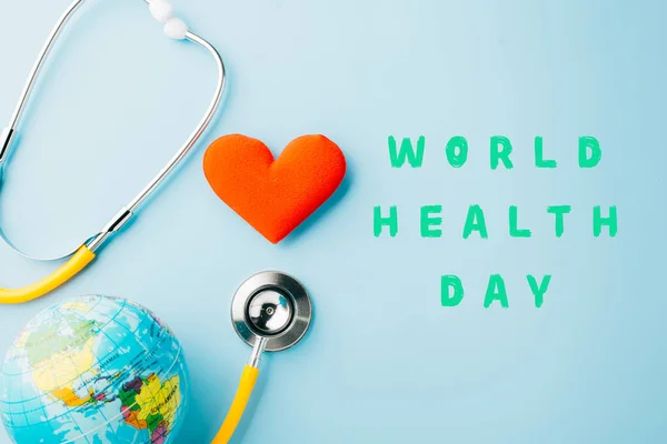 World Health Day. Yellow doctor stethoscope and world globe with Red heart shape isolated on blue background with copy space, Save world day, Healthcare life Insurance, Health care and medical concept