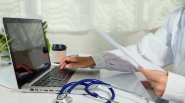 Doctor or nurse woman in uniform with stethoscope working she typing information of patient prescription from paperwork medical history form into laptop computer for record document data report