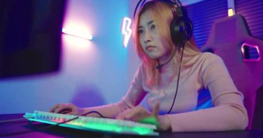 Happy Gamer endeavor plays online video games tournament with computer neon lights, young woman wearing gaming headphones intend to do playing live stream games online at home