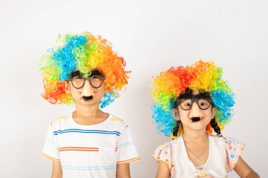 1 Nisan şakası. İki erkek kardeş komik çocuk ve küçük kız palyaço kıvırcık peruk takıyor. Renkli, büyük gözlük takıyor ve beyaz arka planda izole edilmiş bıyıkları var. Mutlu çocuk şenlik dekorasyonu.