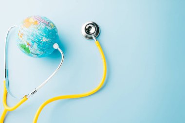 World Health Day. Yellow doctor stethoscope and world globe isolated on pastel blue background with copy space for text, Save world day, Green Earth Environment, Healthcare and medical concept