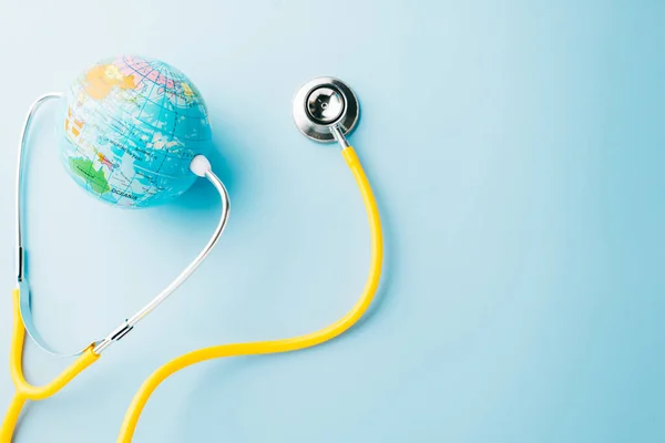 World Health Day. Yellow doctor stethoscope and world globe isolated on pastel blue background with copy space for text, Save world day, Green Earth Environment, Healthcare and medical concept