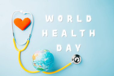 World Health Day. Yellow doctor stethoscope and world globe with Red heart shape isolated on blue background with copy space, Save world day, Green Earth Environment, Healthcare and medical concept