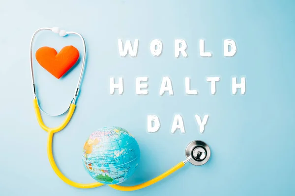World Health Day. Yellow doctor stethoscope and world globe with Red heart shape isolated on blue background with copy space, Save world day, Green Earth Environment, Healthcare and medical concept