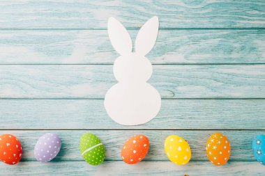 Easter Day Concept. Top view holiday banner background web design white colorful easter eggs and paper bunny rabbit on blue wood background with copy space, celebration greeting, overhead, template