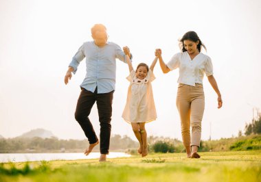 Asyalı bir aile güzel bir bahar parkında yürüyor ve el ele tutuşuyor, doğanın ve birlikteliğin tadını çıkarıyor, mutlu ve neşeli hissediyorlar, mutlu aile günü.