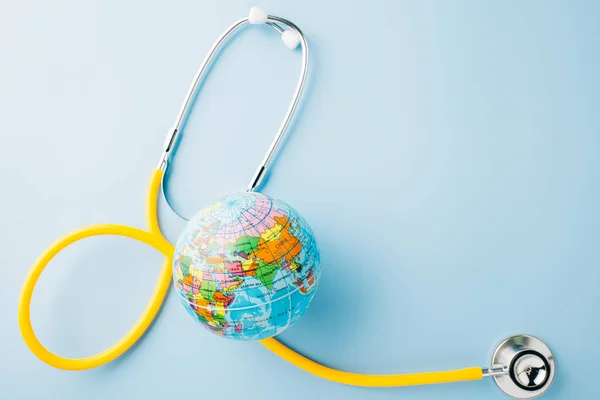 World Health Day. Yellow doctor stethoscope and world globe isolated on pastel blue background with copy space for text, Save world day, Green Earth Environment, Healthcare and medical concept