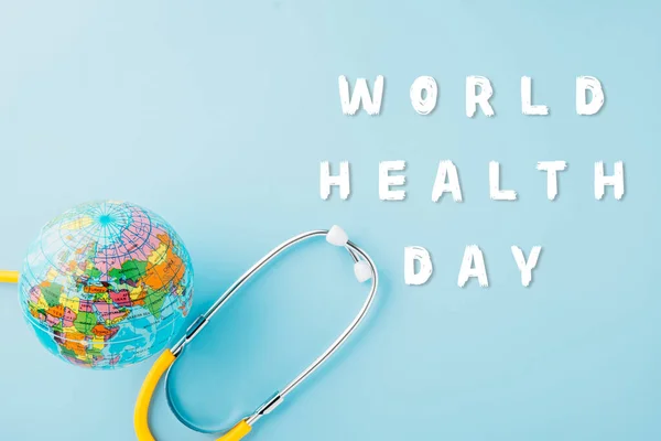 World Health Day. Top view yellow doctor stethoscope wrapped around world globe isolated on pastel blue background with copy space for text, Save world day, Health care and medical concept