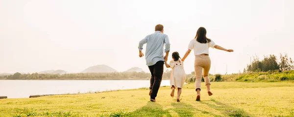 快乐的父亲和女儿在绿草如茵的草地上跑来跑去 背景是夕阳西下 周末全家出游 一家人在一起玩得很开心 — 图库照片