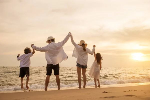 幸せなアジアの家族は 日没時に休暇でビーチで一緒にジャンプする楽しみを持っています 家族のシルエットは ビーチで健康的なライフスタイルを手に 旅行や休暇のコンセプトを楽しんでいる人々をバックアップします — ストック写真