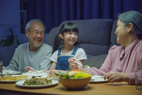 幸せなアジアの家族の祖母の祖父と孫娘はテーブルで食事をし 家庭の夜の時間に楽しい時間を過ごして シニア親と子供は屋内で一緒にリビングルームで一緒に食べ物を食べる — ストック写真