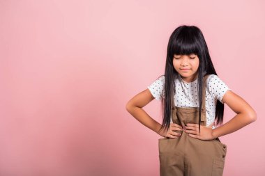 Asian little kid 10 years old suffering from stomach ache at studio shot isolated on pink background, Happy child girl hand hold stomach pain because indigestion, painful illness feeling unwell