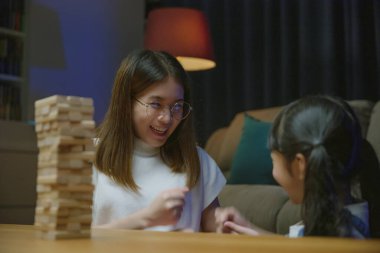 Gülen kadın, çocuklara tahta blokların yapımcılığını öğretiyor. Asyalı genç anne, gece yatmadan önce küçük kızıyla birlikte tahta blokta oyun oynuyor.