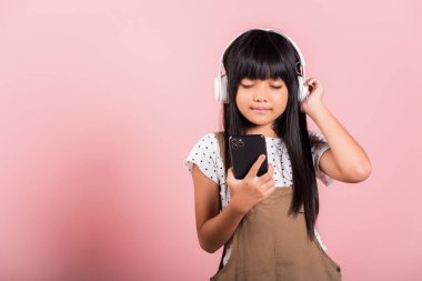 Asyalı çocuk 10 yıl boyunca cep telefonundan müzik dinledi. Stüdyoda kablosuz kulaklık taktı. Pembe arka planda izole edildi.