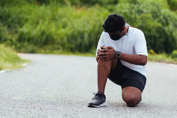 在室外街道健康公园跑步时 亚洲年轻的运动健将黑衣人身穿手表 手牵着膝盖疼痛 运动理念对健康的伤害 — 图库照片