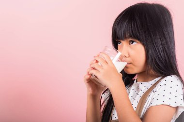 Asyalı küçük çocuk 10 yaşında gülümsüyor süt bardağı tutuyor beyaz süt içiyor ve pembe arka planda izole edilmiş bir şekilde stüdyoda içiyor mutlu çocuk günlük sağlık sigortası yemekleri yiyor.