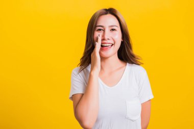 Asya Taylandlı mutlu bir portre güzel bir kadın tişört giyer dudaklarına el ele tutuşur gizli dedikodular fısıldar izole edilmiş fotoğraf stüdyosuna bakar sarı arka planda fotokopi çekilir