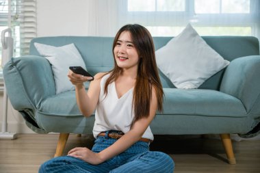 Asyalı genç bir kadın gülümsüyor. Oturma odasında televizyon seyrediyor. Uzaktan kumandalı koltuklar tutuyor.