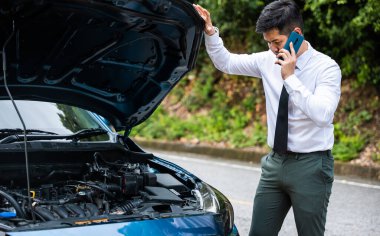 Otoyolda duran zarif iş adamı, araba motor sorunlarını analiz ediyor. Orta yaşlı bir adam sinirli bir ifadeyle motoru incelemek için eğiliyor. Araba tamiri ve bakım konsepti.