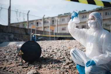 Nehirden çıkan zehirli kimyasalları test tüpü camlarıyla test eden ve beyaz duman çıkaran ekolojist, koruyucu kıyafet giyiyor ve maske endüstriyel, sorunlu ortamdan örnek su topluyor.