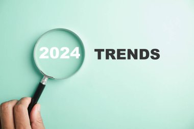 Görüntü, başlıca değişim eğilimini vurgulayarak, 2024 Yeni Yıl Trendleri metninin yer aldığı büyüteçler içeriyor. Değerlendirme yöntemleri, popüler konular ve iş dünyasındaki yeni eğilimleri temsil etmektedir..