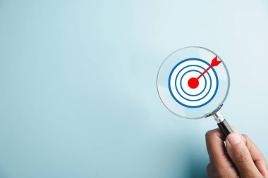 Büyüteç bir hedef tahtası üzerine kurulur, ticari amaçların önemini gözler önüne serer, arama, hedef belirleme, strateji ve başarı kavramlarını temsil eder.