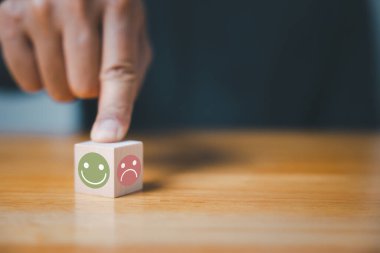 Bir iş adamının eli, en iyi müşteri deneyimi için tahta bir gülen yüz seçer. Memnuniyet araştırması ve geri bildirim konsepti. 5 yıldızlı memnuniyet garantilidir..
