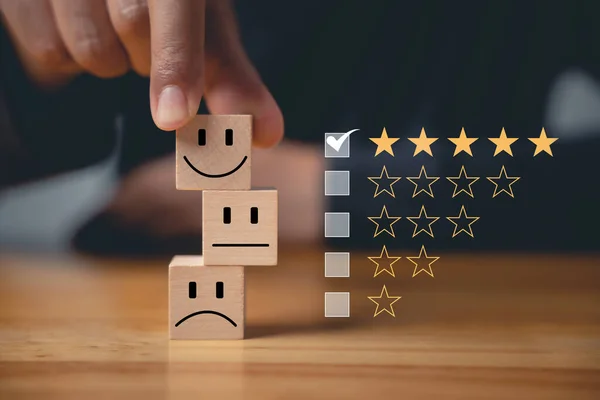 5-star satisfaction is guaranteed with a wooden block cubes smiley face selected by a businessmans hand. Satisfaction survey and feedback concept for the best customer experience.