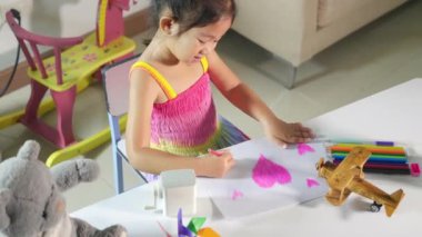Asyalı şirin çocuk anaokulunda gülümsüyor yaratıcı kalpler çiziyor evde aşk resmi çekiyor mutlu çocuk renkli küçük kız beyaz kağıda pembe kalp çiziyor sevgililer günü ya da anneler günü ya da babalar günü, sanat eğitimi.