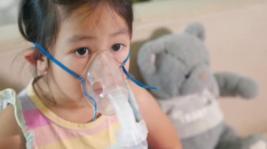Kid girl making makes inhalation nebulizer steam sick cough at home, Asian Child using nebulizer mask equipment alone have smoke, stuffy nose and runny, oxygen spray inhaler therapy, Health medical