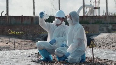 Nehirden çıkan zehirli kimyasalları test tüpü camlarıyla test eden ve beyaz duman çıkaran ekolojist, koruyucu kıyafet giyiyor ve maske endüstriyel, sorunlu ortamdan örnek su topluyor.