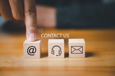 Web sitesi sayfası bizimle ya da e-posta pazarlama konseptiyle iletişime geçin. Müşteri destek hattı insanları birbirine bağlıyor. E-posta, telefon, adres ve kulaklık ikonlarıyla ahşap küp. Kurumsal iletişim çözümü.