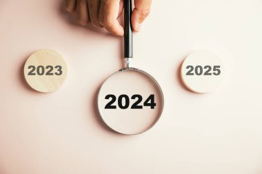 2024 simgesine odaklanan bir büyüteç, önümüzdeki yıl için hedef sektörü vurguluyor. 2023 'ün sonundan yeni yıl konseptine geçiş yapan planlama, yenilik ve yatırım fikirlerini sembolize eder..