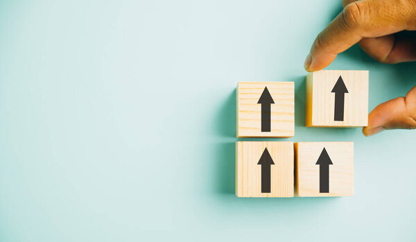 Business growth concept depicted by male hands stacking wooden blocks as steps. An arrow pointing upwards represents the rise in value, revenue, and success. Copy space provided for customization.