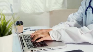 Closeup of doctor or nurse woman in uniform with stethoscope typing information of patient prescription from paperwork medical history form into laptop computer for record document data report