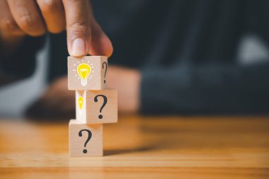 İş desteği ve yenilik stratejisi. Ampul ikonu ve soru işareti olan ahşap bir blokla el ele tutuşmak. Yaratıcı çözüm ve başarı için yeni fikirler. Uzman danışmanlık ve anlayış.