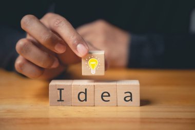 Uzman danışmanlığı ve yaratıcı çözüm konsepti. Ampul ikonlu ahşap blokla el ele tutuşmak. Yeni fikirlerin ve yenilik stratejisinin geliştirilmesi. Yaratıcı hayal gücüyle iş başarısı.