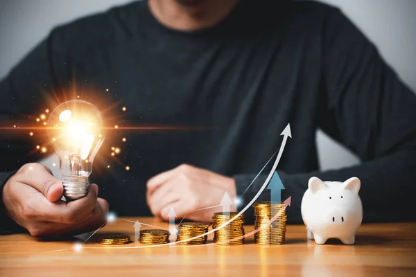 手握一个装有硬币堆栈和图表的灯泡 代表了省钱和投资于财富的创意理念 商业会计的财务背景 创新和聪明 — 图库照片