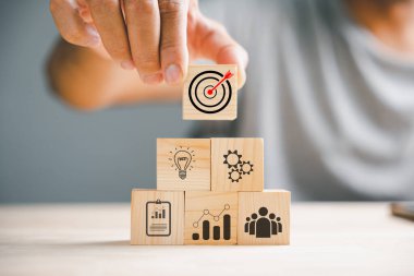 İşadamları ahşap blokları titizlikle düzenleyerek bir iş stratejisi ve eylem planını sembolize ediyorlar. Pazarlama ve tanıtım kavramı hedefleniyor.