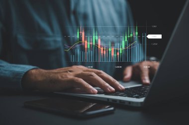 Evdeki bir tüccar veya yatırımcı, teknik fiyat grafikleri, şamdan grafikleri ve ticaret göstergelerini gösteren bir dizüstü bilgisayar ekranında borsa işlemlerini yürütüyor ve analiz ediyor..