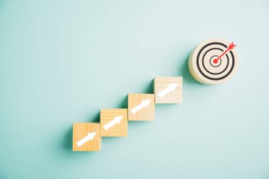 Hedef simge tahta bloklara entegre edildi. Yükselen oklar iş büyümesini resmediyor. Çubuk grafik çizelgesi mavi bir arkaplan üzerinde adımlar kâr, yatırım ve ekonomik gelişimi sembolize eder.