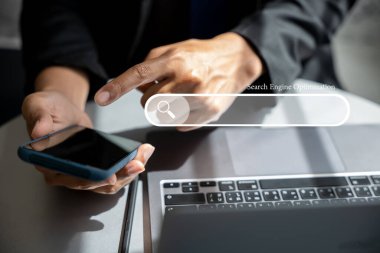 İş adamı SEO araçları için akıllı telefonu müşteri bulmak ve içeriği çevrimiçi olarak tanıtmak için kullanıyor. Dijital pazarlama ve iş teknolojisi konsepti. Arama çubuğuyla arama motoru optimizasyonu