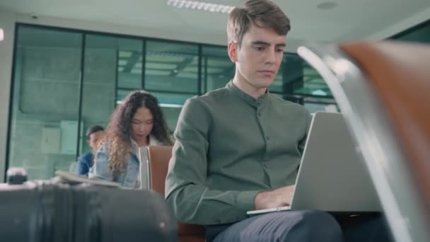 Junger Gutaussehender Mann Mit Koffer Sitzt Seinem Laptop Der Flughafenhalle — Stockvideo