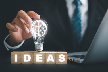 İlham ve yaratıcılık. Bir adamın eli, ahşap bloktaki fikirlerin yanında bir ampul tutar. Yenilik konseptini, iş girişimlerini gözler önüne seriyor. Yaratıcı düşüncenin gücünü simgeler..