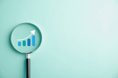 Tüccar, çubuk grafiğini yükselen okla incelemek için büyüteç kullanıyor. Teknik borsa grafiğinin analizi, potansiyel büyüme ve başarı için iş yatırımı kavramını somutlaştırıyor.