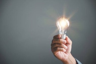 Bir insanın ampul tutarken, yaratıcı düşünme, yenilik ve çözüm odaklı yaklaşımları somutlaştırdığı ilham verici bir görüntü. Bu fikir iş başarısını güçlendirir..