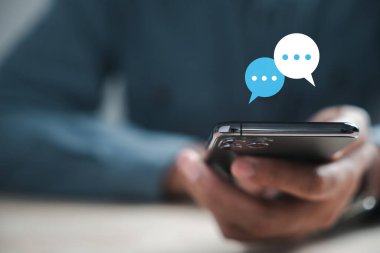 Erkekler canlı sohbet ve sosyal ağ kavramlarını yazmak için akıllı telefon kullanır. Evde sohbet, sohbet kutusu simgeleri ortaya çıkıyor, modern iletişim ve sosyal medya pazarlamasını betimliyor.