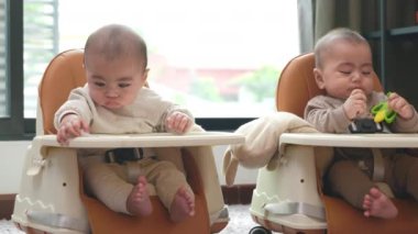 Emniyet sandalyesinde oturan Asyalı ikiz bebekler, koltuklar araba koltukları için kullanılabilir, evde yemek yemek için bekleyen iki küçük bebek.